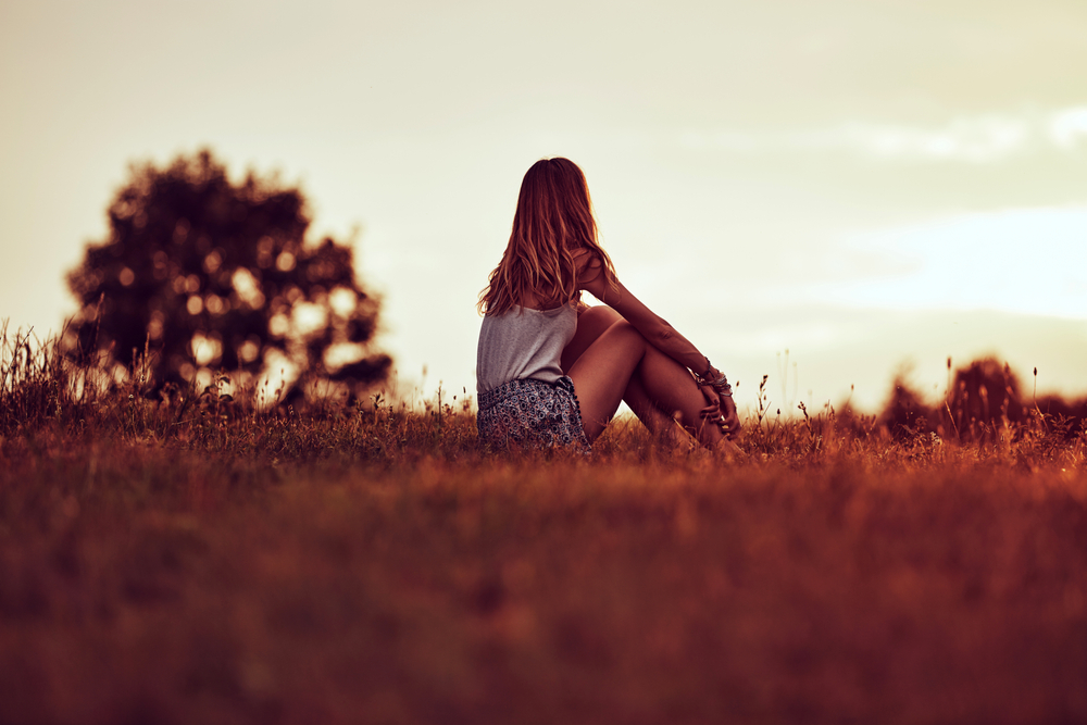 A woman sitting in a field thinking in the sunset